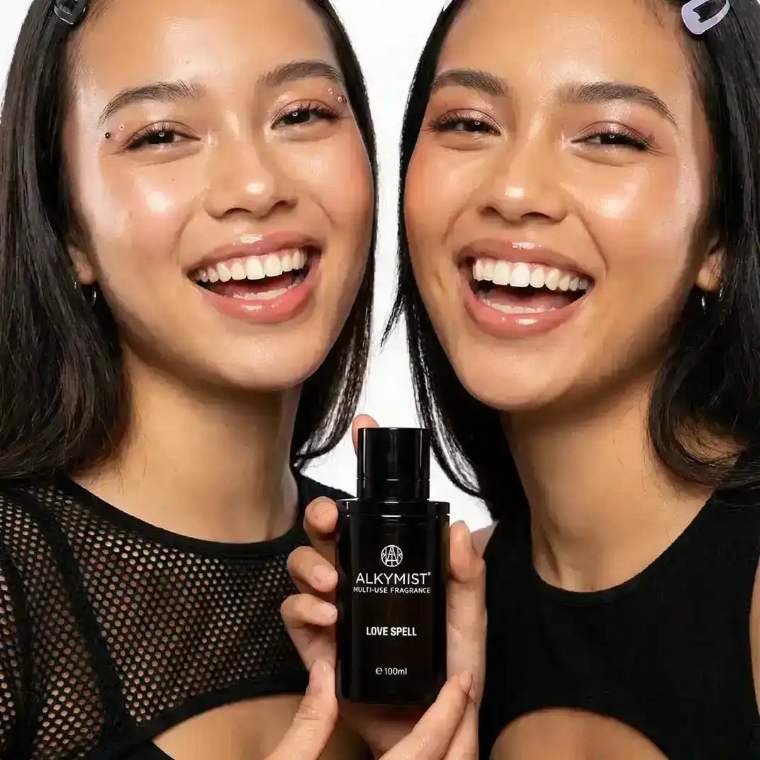 Two women smiling and holding AEMBR ALKYMIST Love Spell fragrance bottle, clean beauty