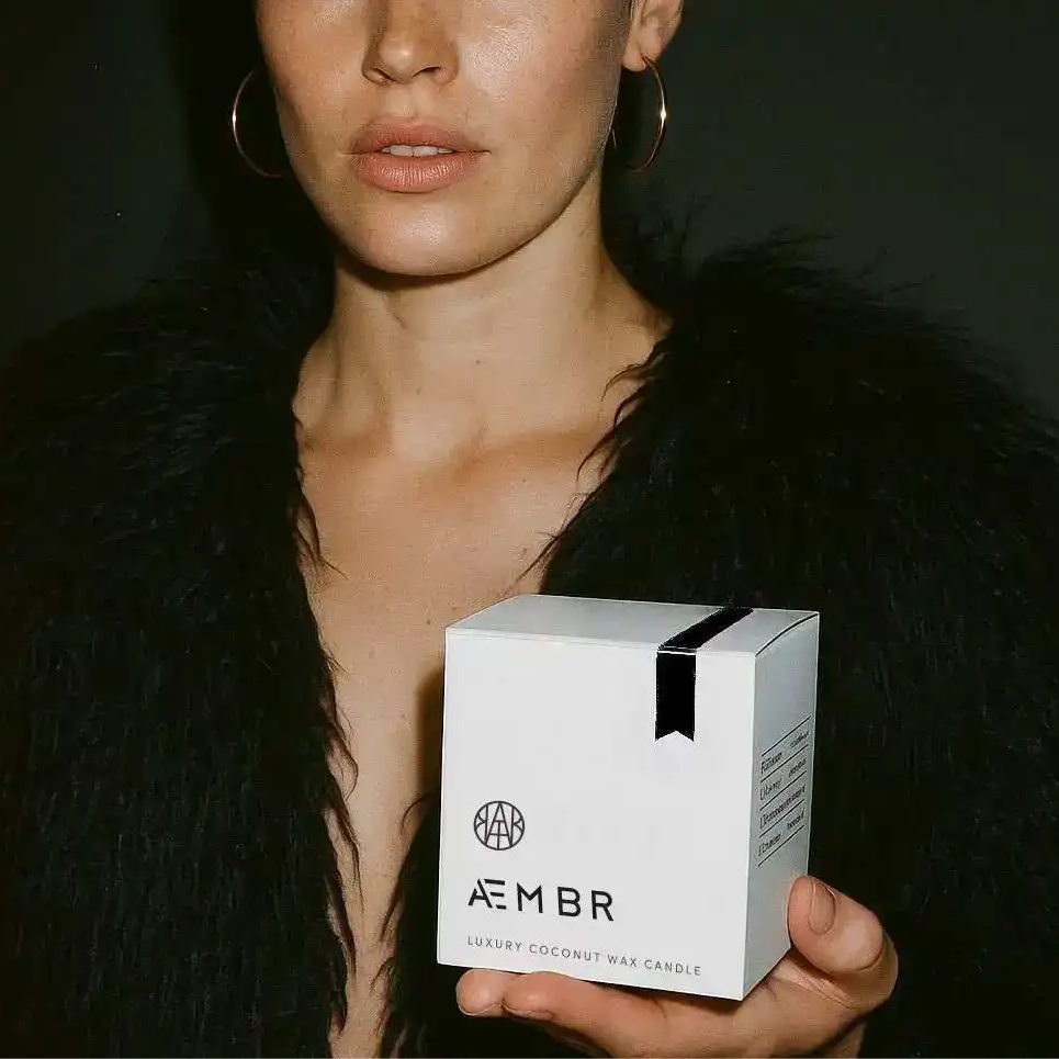 Woman holding AEMBR luxury coconut wax candle box, non-toxic home fragrance brand