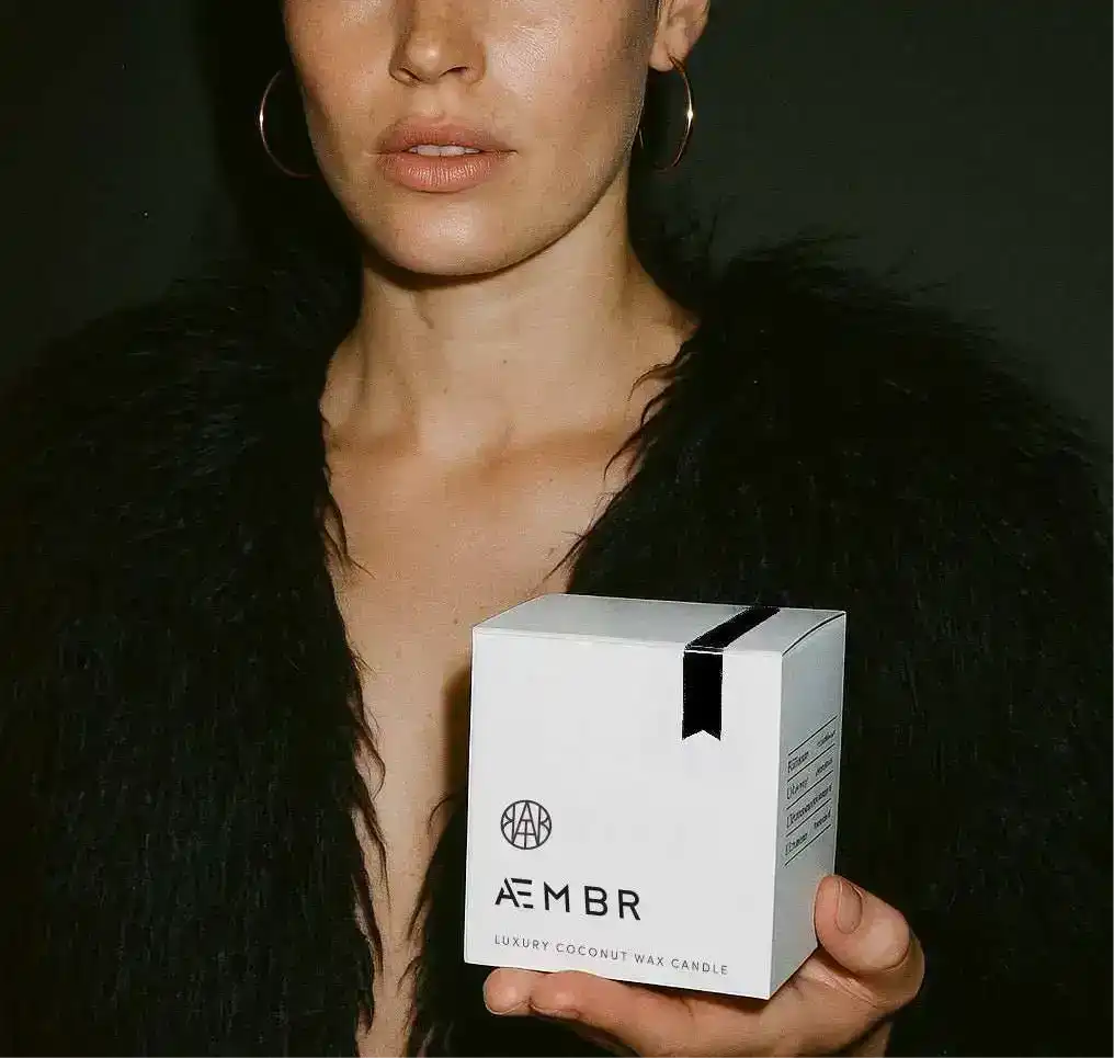 Woman holding non-toxic luxury coconut wax candle box against dark background