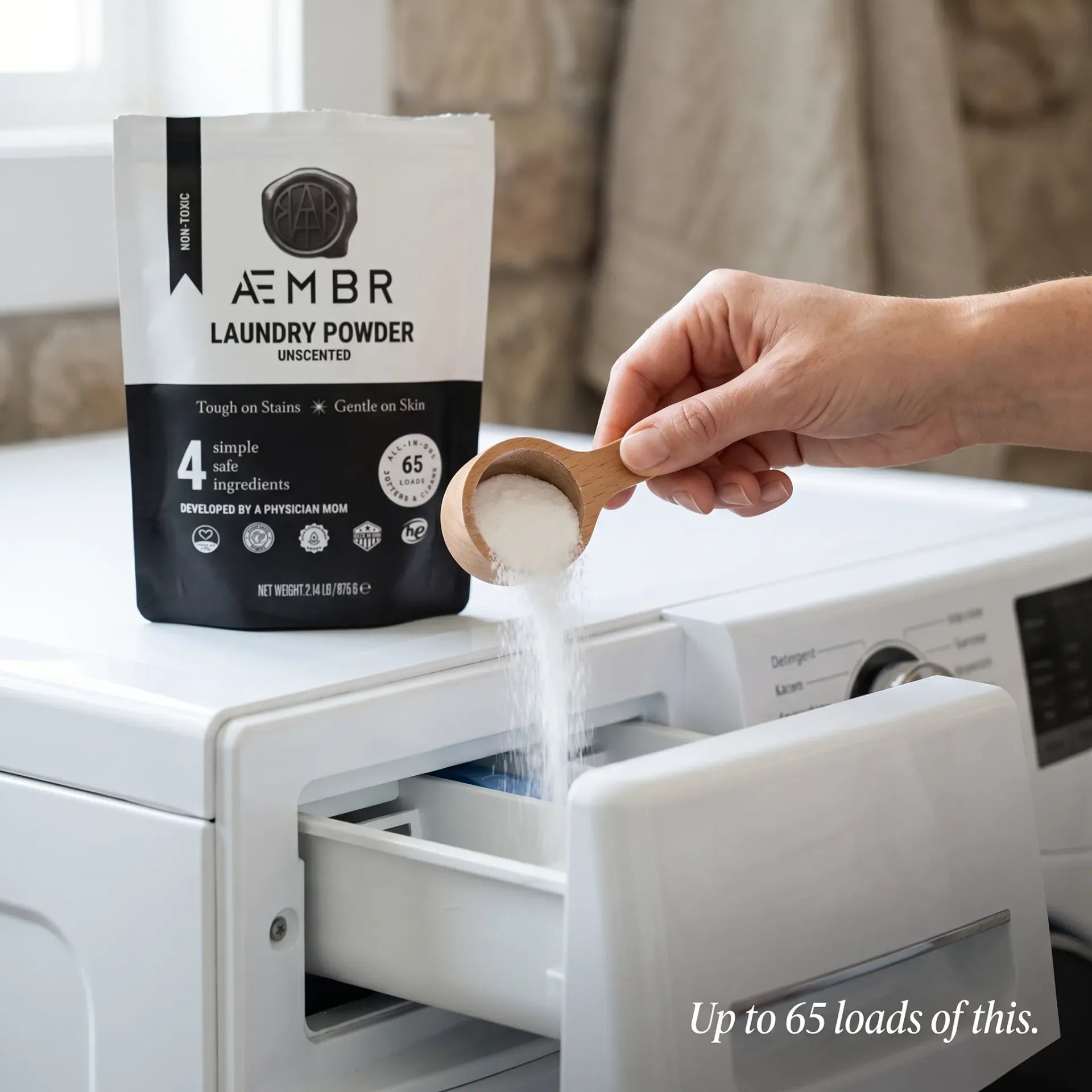 AEMBR Laundry Powder being scooped with wooden laundry scoop into washer detergent drawer — up to 65 loads, non-toxic concentrated clean