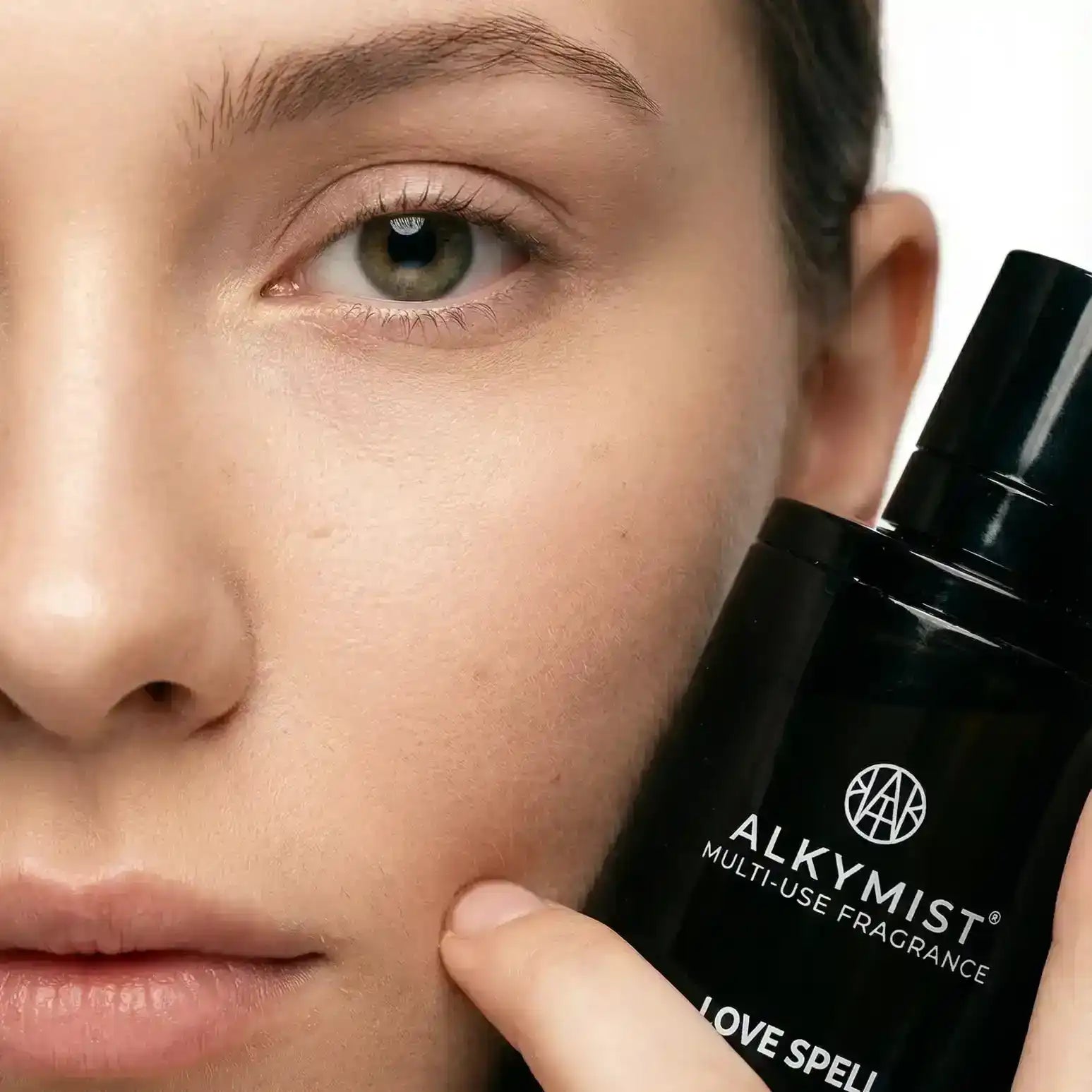 Close-up of a person holding AEMBR ALKYMIST multi-use fragrance bottle by their face