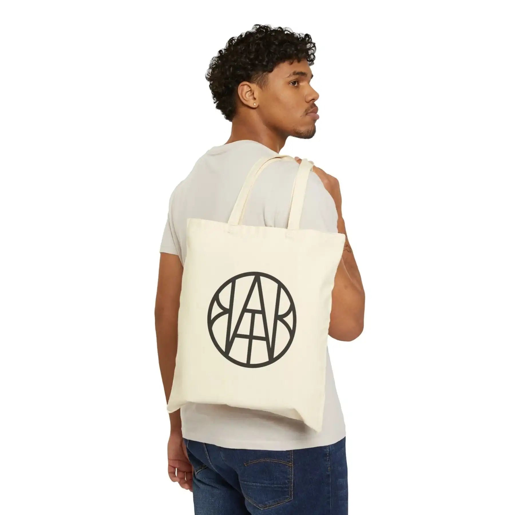 Man carrying AEMBR branded canvas tote bag with black circular logo, minimalist style