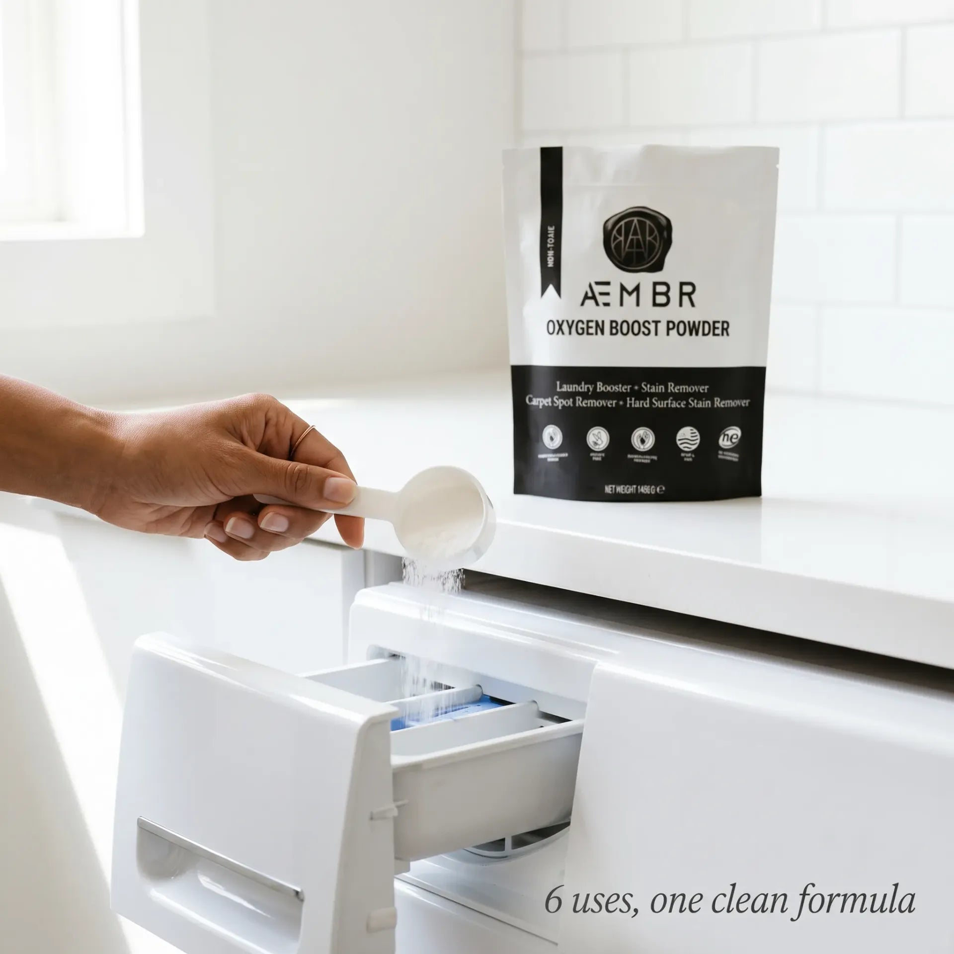 AEMBR Oxygen Boost being poured into washing machine drawer with scoop — 6 uses, one clean formula, fragrance-free non-toxic laundry powder