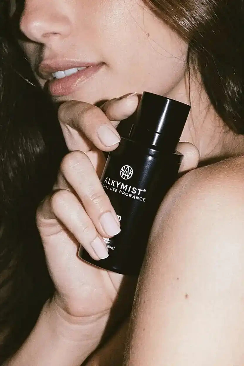 Woman holding ALKYMIST non-toxic fragrance bottle close to bare shoulder