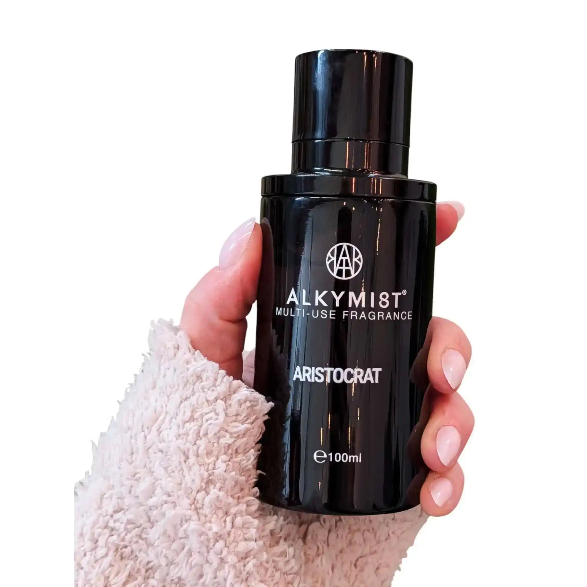 Hand holding black bottle of non-toxic multi-use fragrance spray, 100ml size, white background