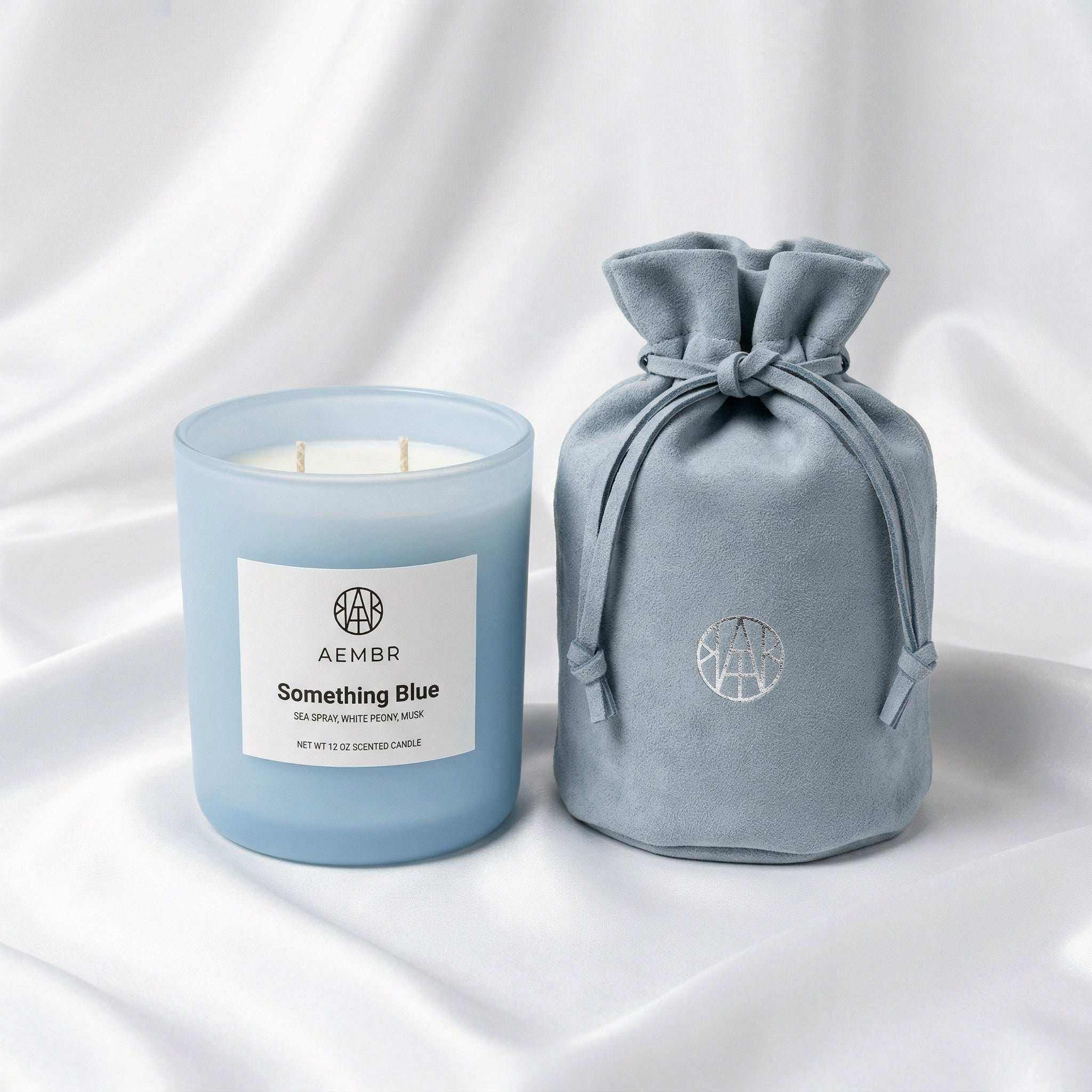 Non-toxic Something Blue scented candle in frosted blue jar with matching gift pouch on white fabric.