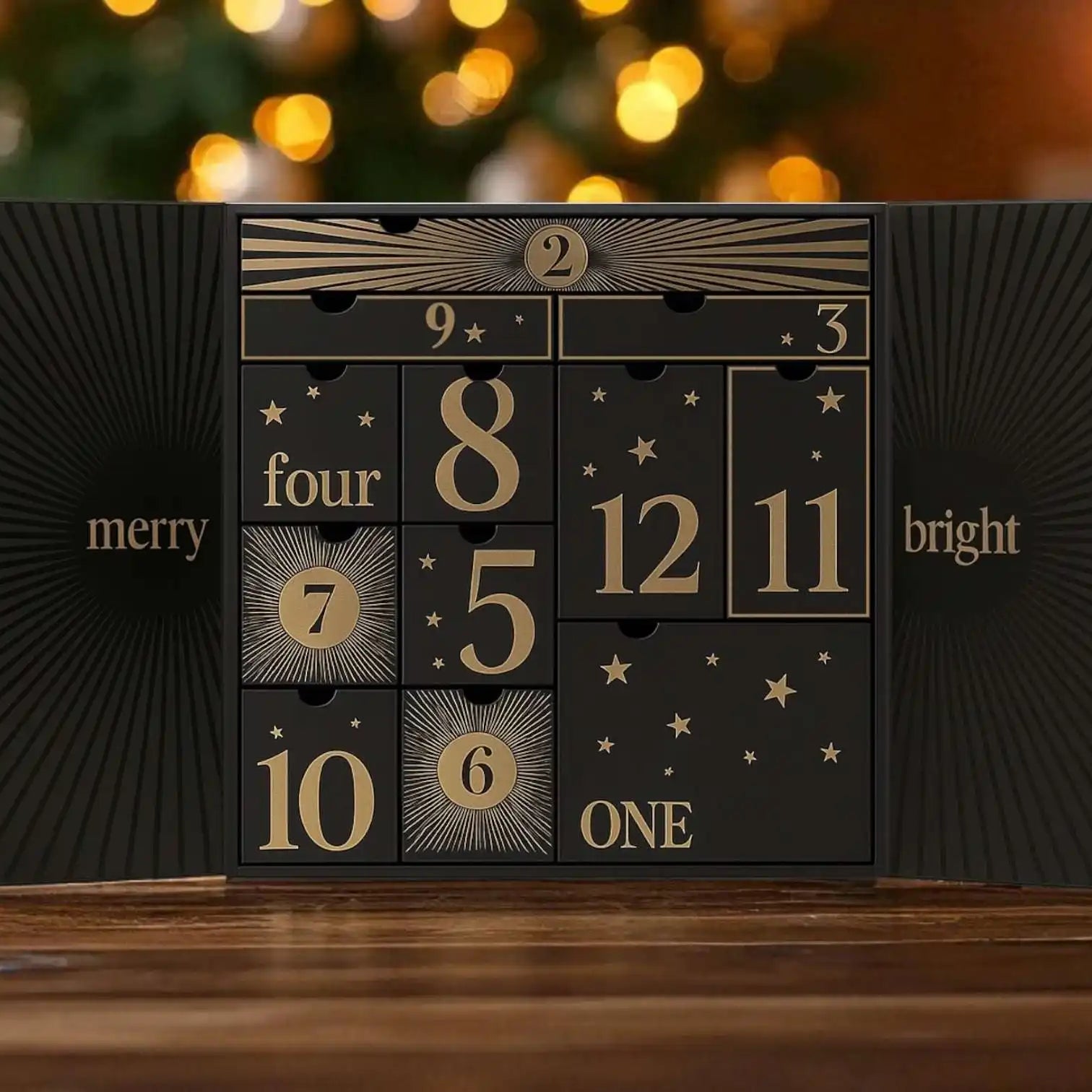 AEMBR black and gold Advent calendar open on table, holiday lights and tree blurred in background.