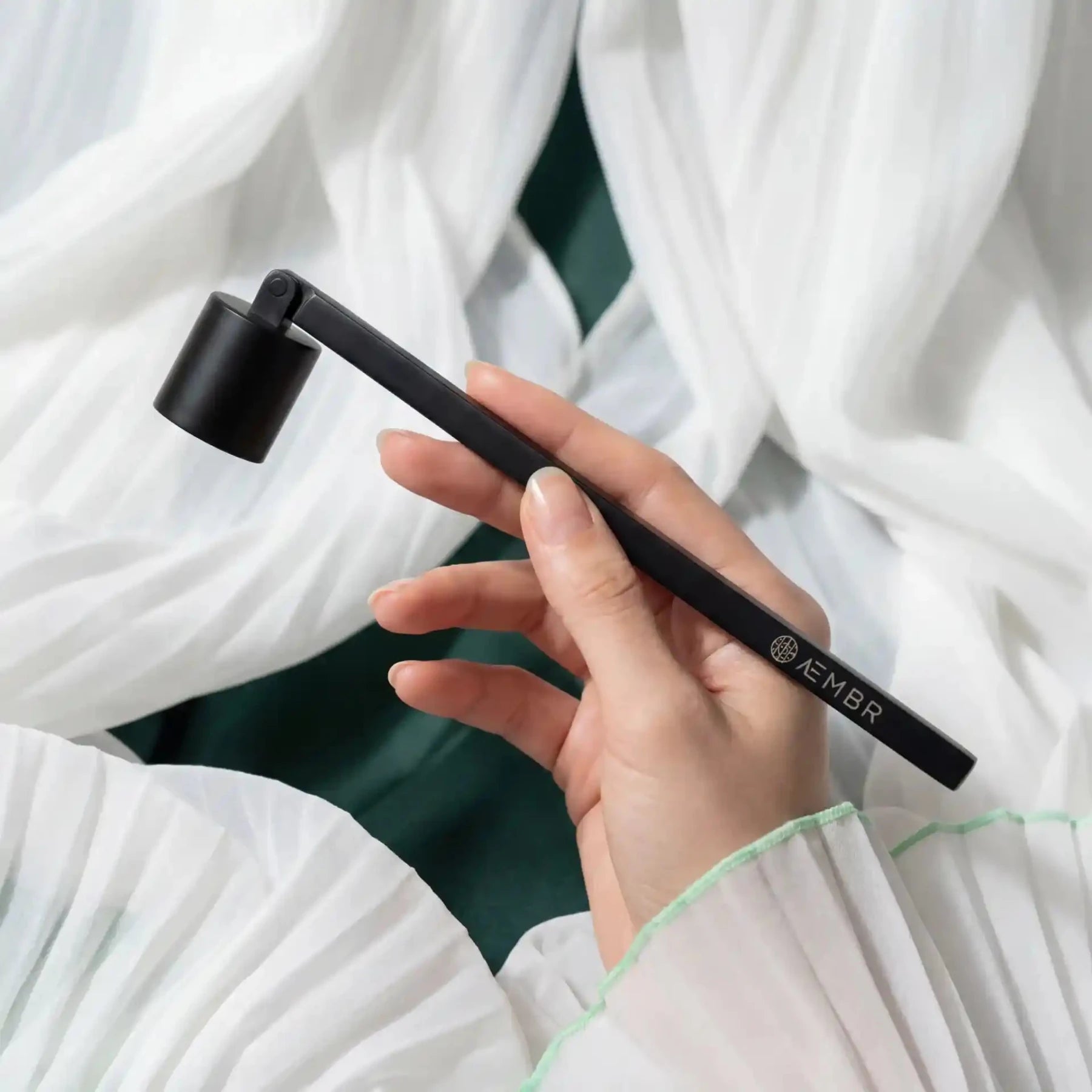 AEMBR candle snuffer in black metal, designed for safely extinguishing candles with a long handle and bell-shaped top.