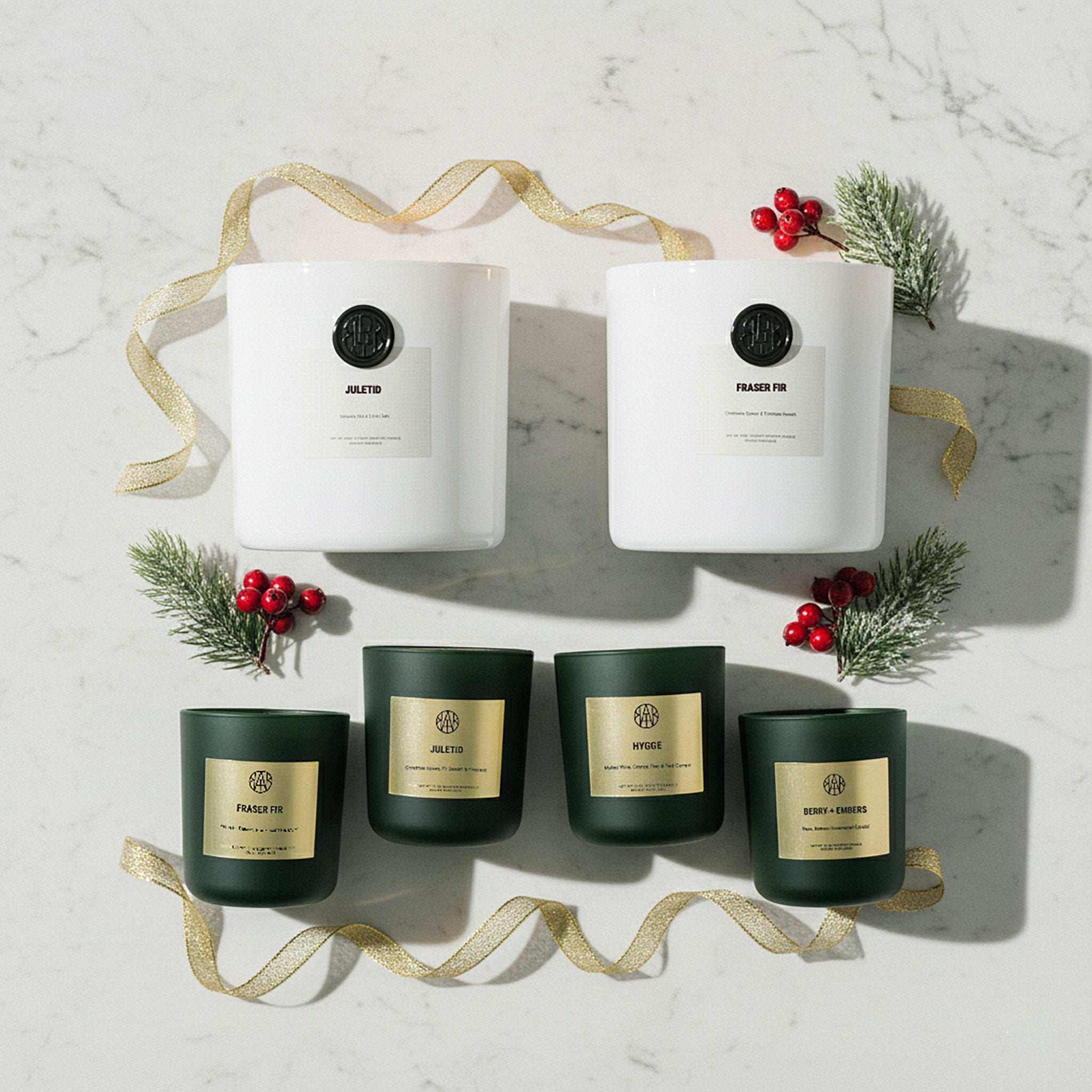 Non-toxic winter collection candles in white and green jars with holiday decor on marble surface