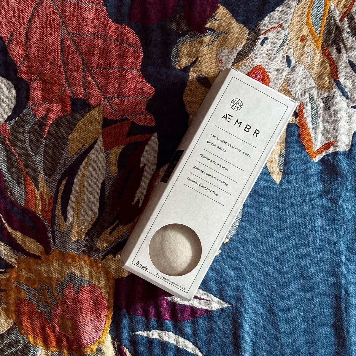 AEMBR wool dryer balls box on a colorful floral-patterned blanket, eco-friendly home care
