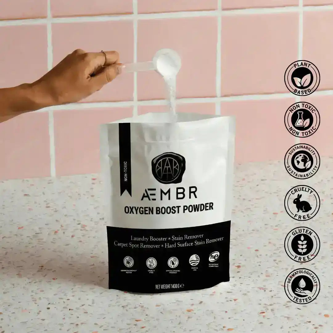 AEMBR Oxygen Boost laundry additive in a container with dryer balls, linen spray, and detergent scoop for fresh, clean laundry.