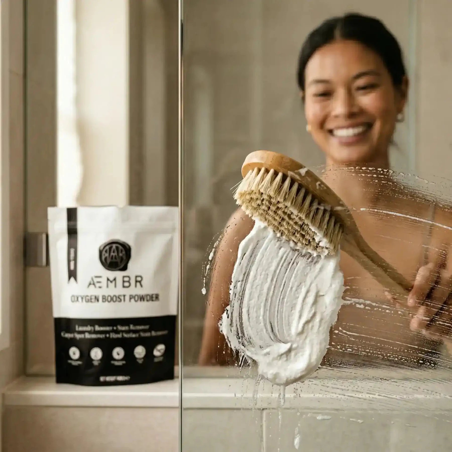 AEMBR Oxygen Boost laundry additive in a clear bottle with a scoop, surrounded by detergent, dryer balls, linen spray, and natural scents.