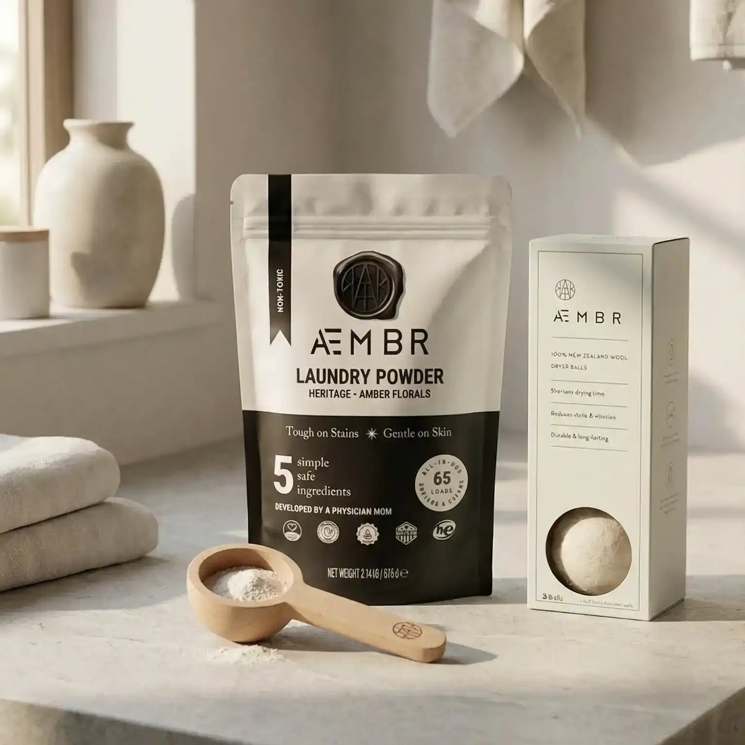 AEMBR non-toxic laundry powder and wool dryer balls bundle on a neutral countertop