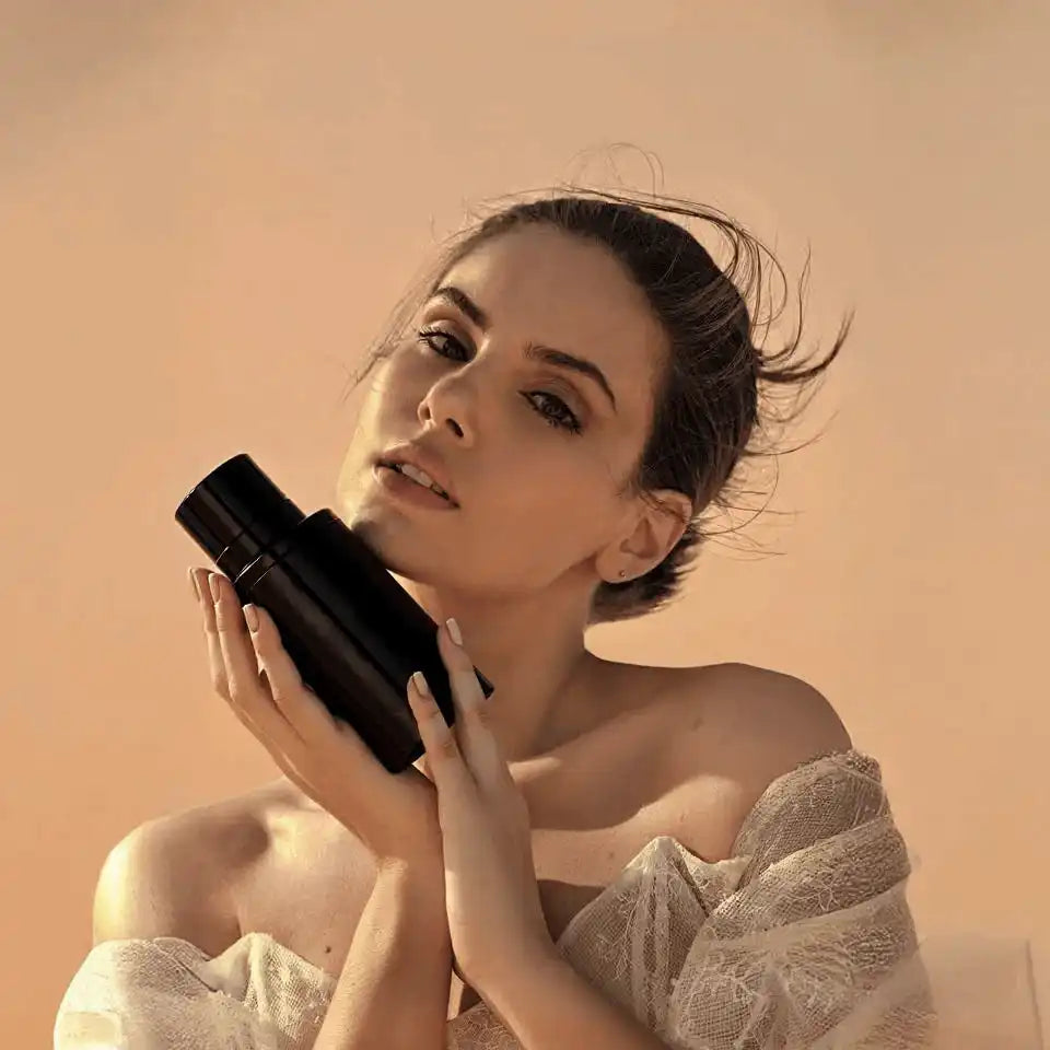 Woman holding AEMBR Alkymist bottle in soft natural light, promoting non-toxic home products