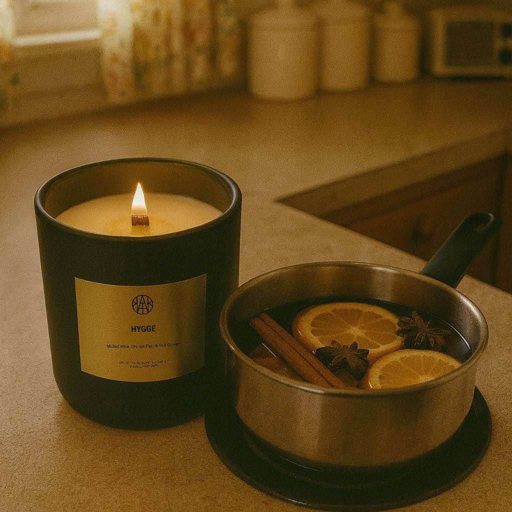AEMBR Hygge candle burning beside a pan of mulled wine with orange slices and spices on a cozy kitchen counter.