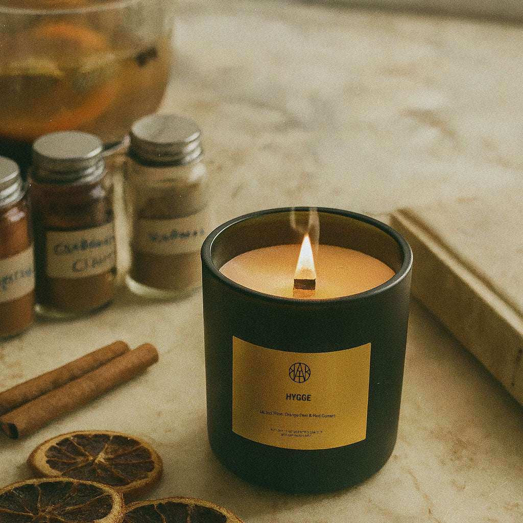 AEMBR Hygge candle in black jar on marble with dried orange slices, spices, and cinnamon sticks