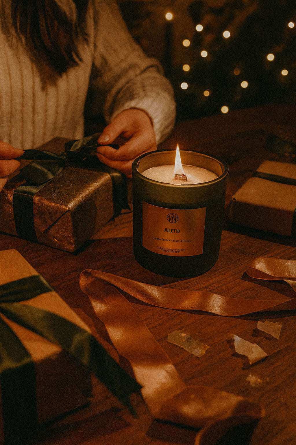 AEMBR Juletid candle burning on a table with wrapped gifts and festive ribbon in warm lighting
