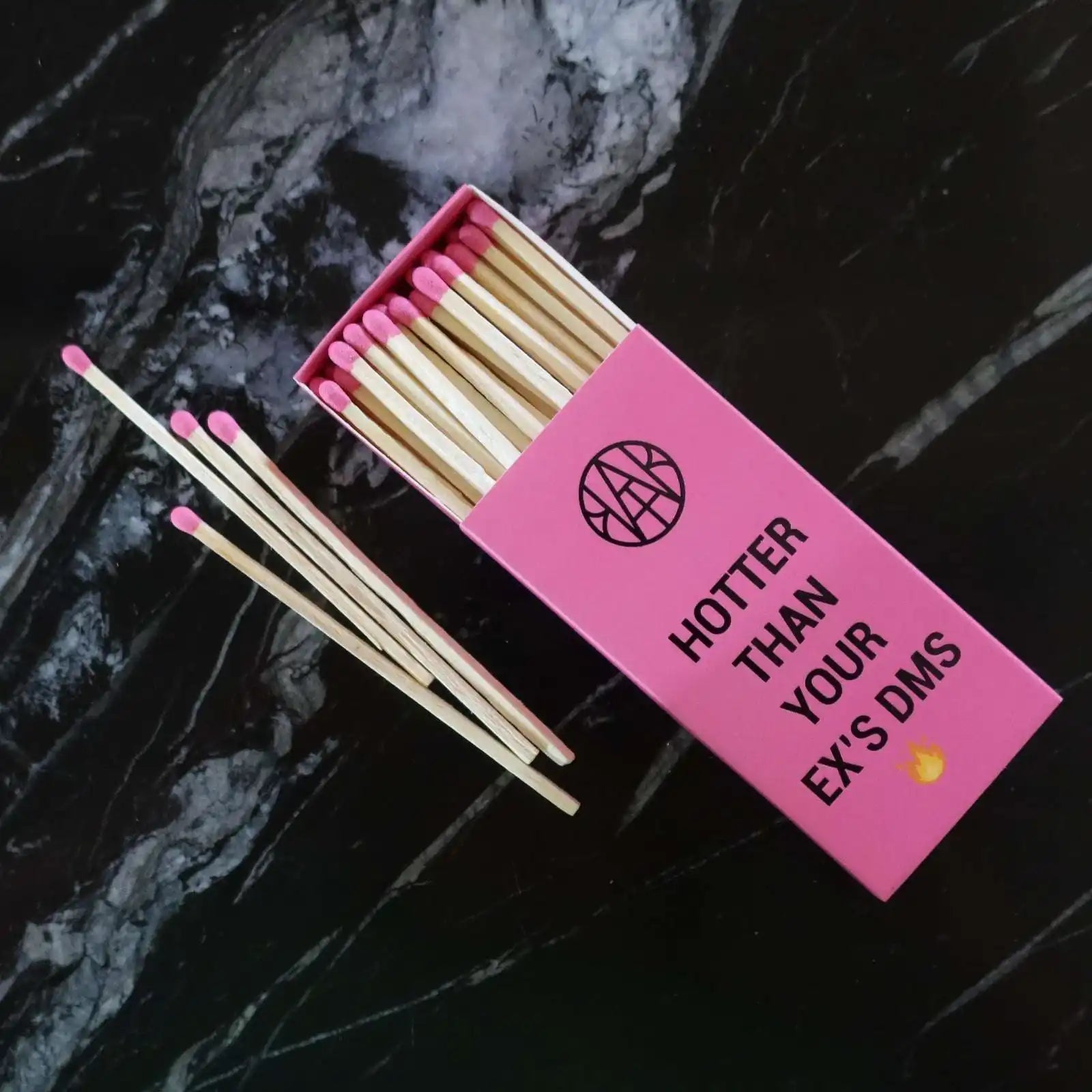 AEMBR pink matchbox with playful slogan and pink-tipped matches on black marble surface.