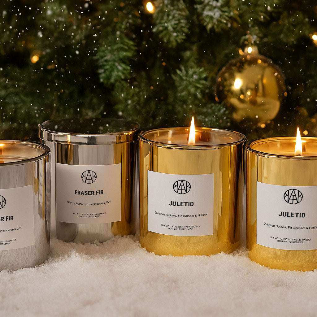 AEMBR silver and gold scented candles burning on snow with a Christmas tree background