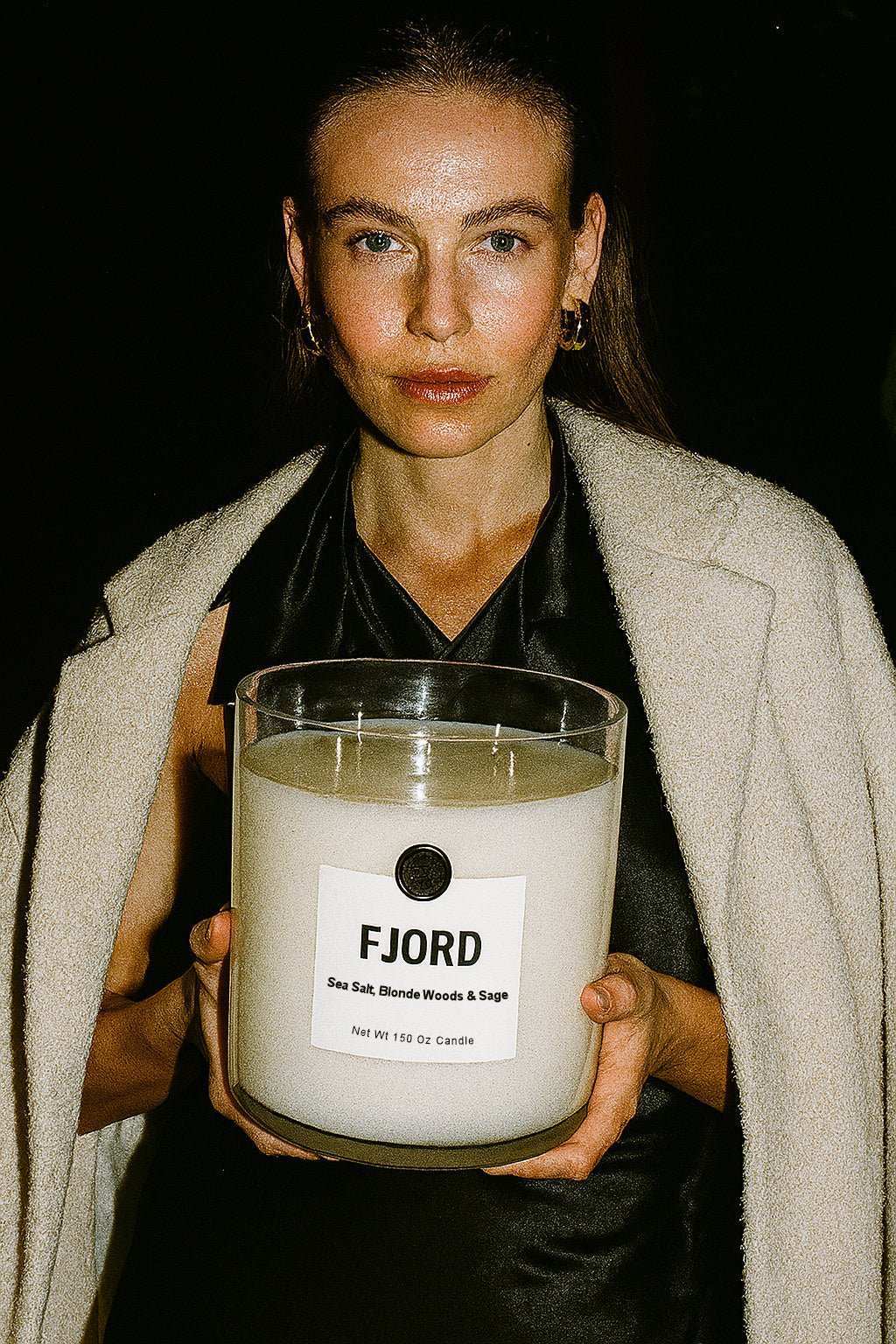 Woman holding large AEMBR FJORD candle with sea salt, blonde woods, and sage label