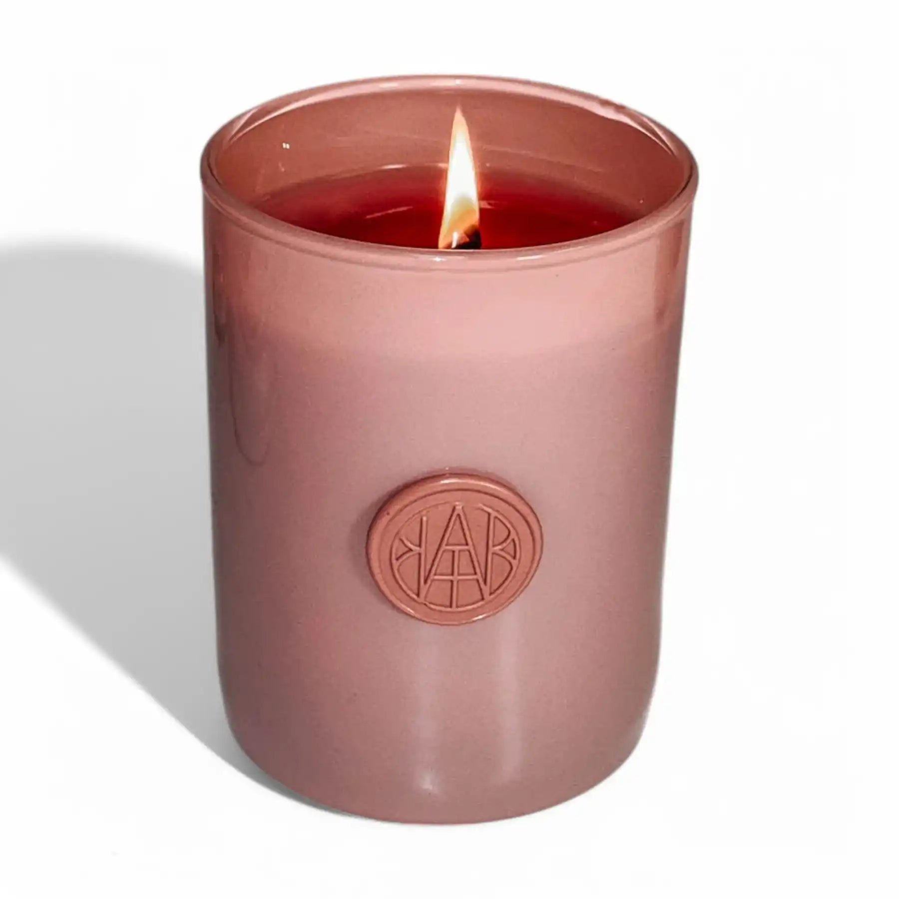 Non-toxic wooden wick candle in pink glass jar with embossed seal, lit on white background