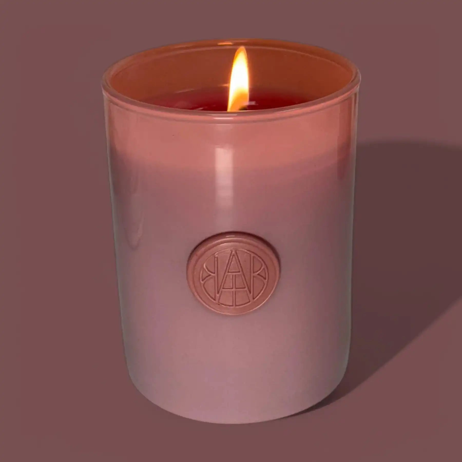 Non-toxic wooden wick candle in mauve glass jar with embossed seal, burning softly