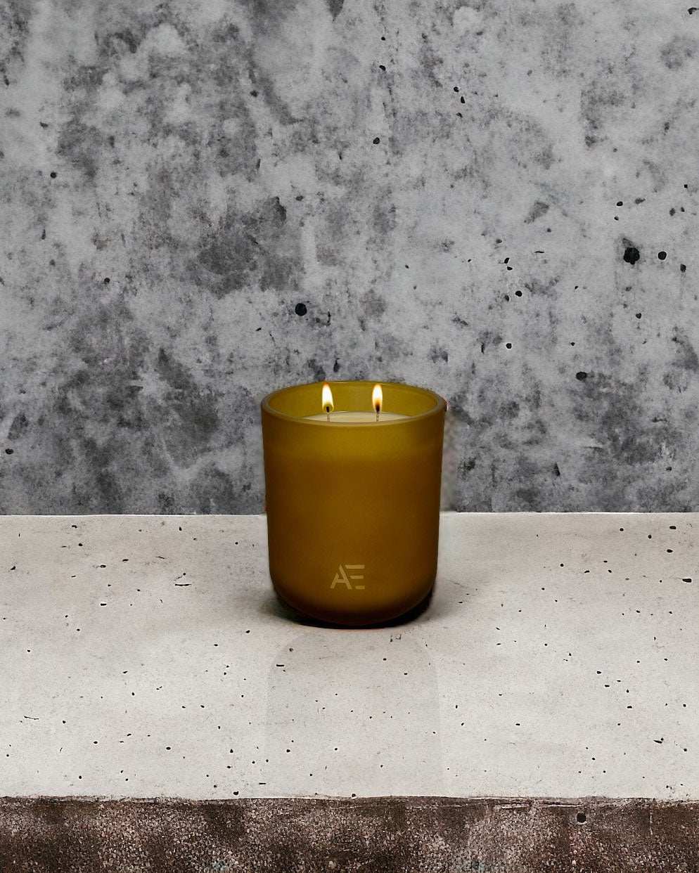AEMBR non-toxic double-wick candle in matte amber glass on concrete surface