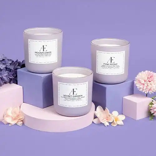 Non-toxic scented candles in glass jars with floral accents, pastel blocks, and purple background