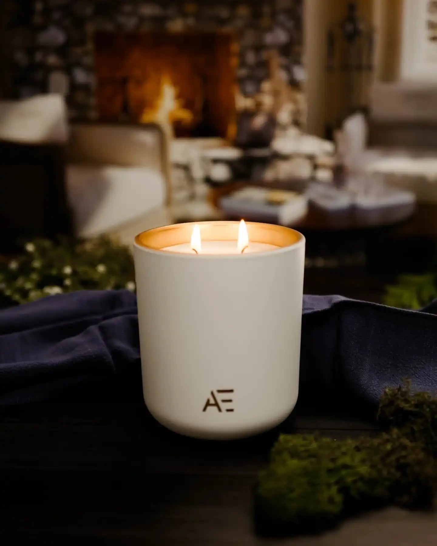 Non-toxic white candle with AE logo burning in cozy living room setting