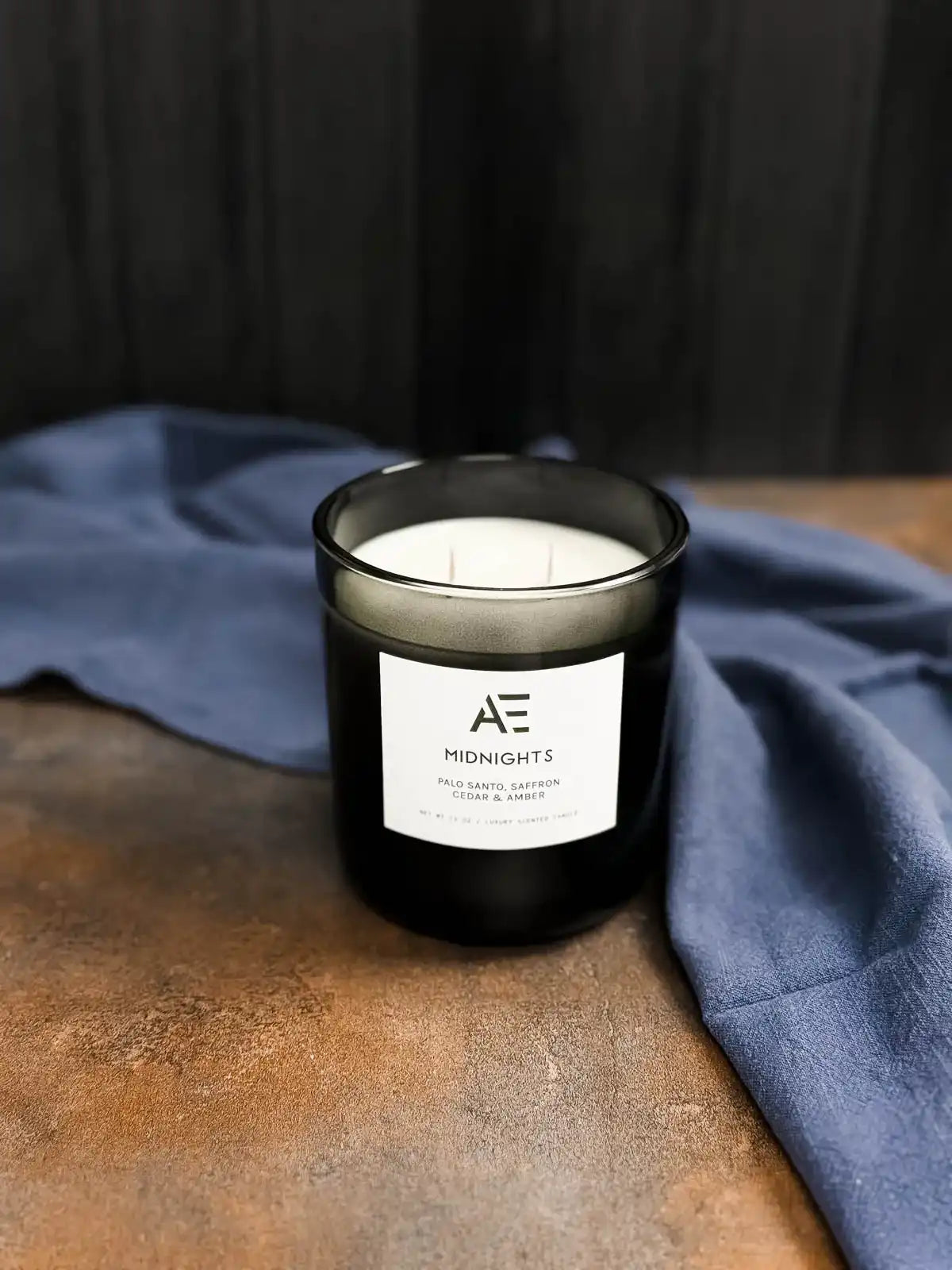AEMBR Midnights black glass candle on brown surface with blue fabric, luxury nontoxic home scent