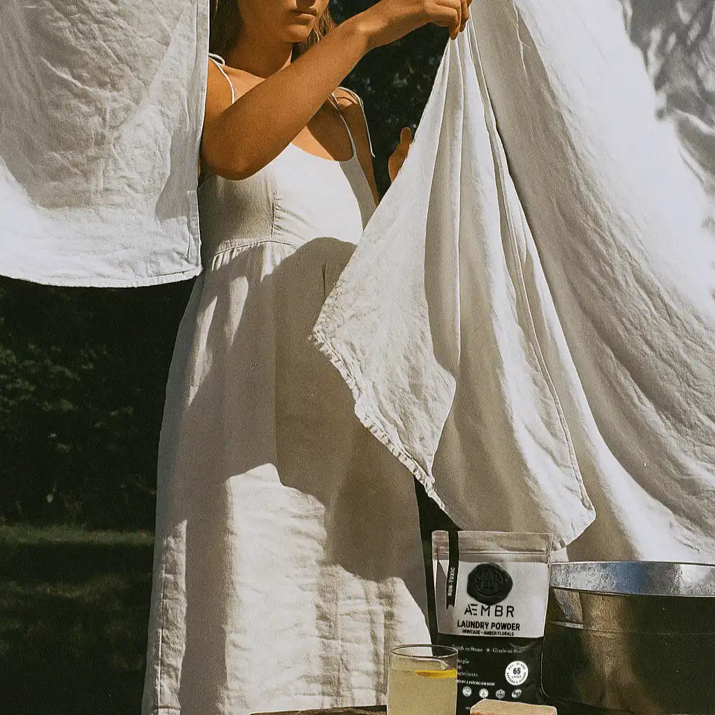 Woman hanging white laundry outdoors with AEMBR non-toxic laundry powder and metal wash tub