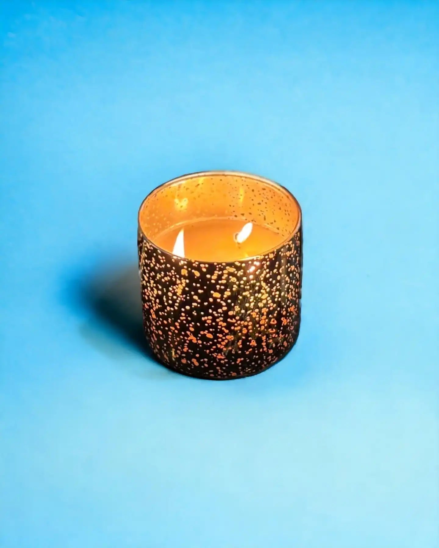 AEMBR decorative lit candle in a gold-speckled glass on a blue background
