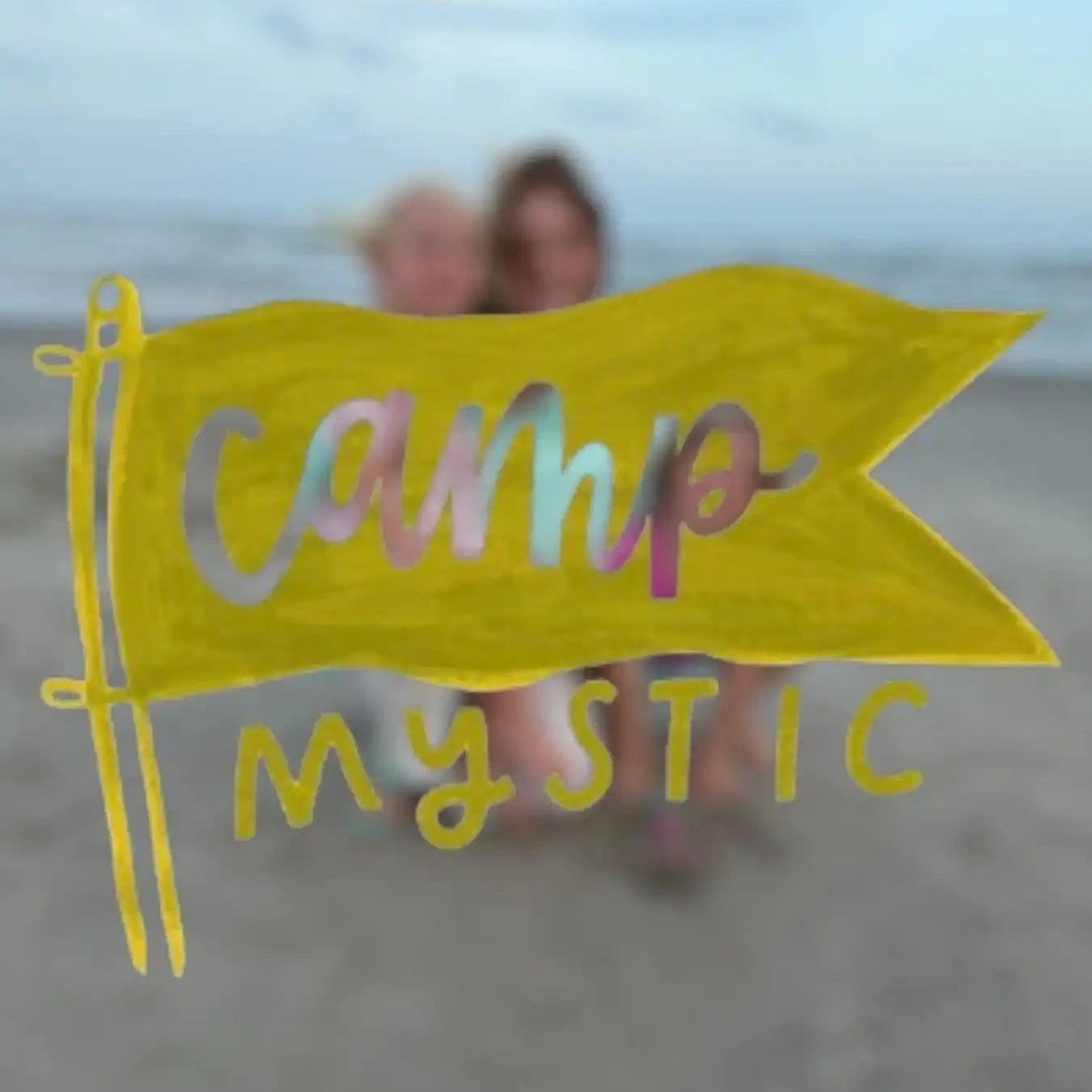 Yellow Camp Mystic flag on beach with two blurred people, AEMBR lifestyle inspired.