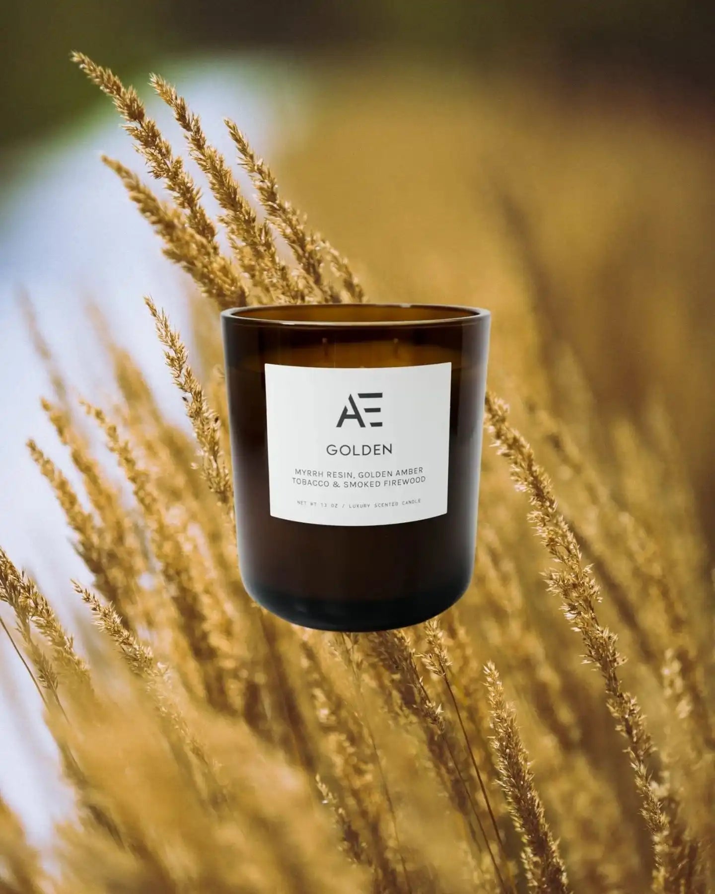 AEMBR Golden scented candle with brown glass jar in front of golden wheat field background