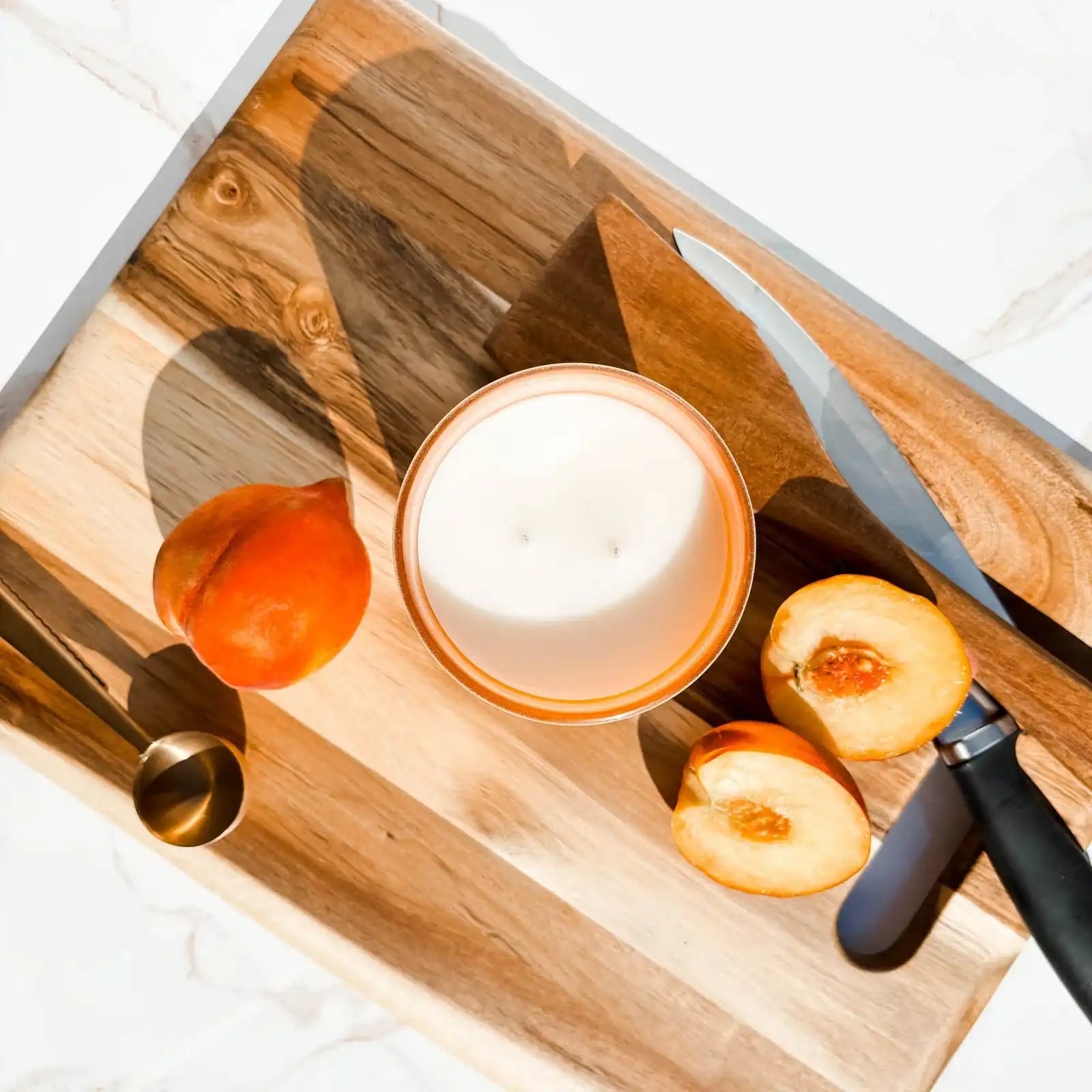 Peach, peach-scented candle, and knife on wooden board, non-toxic home fragrance by AEMBR.