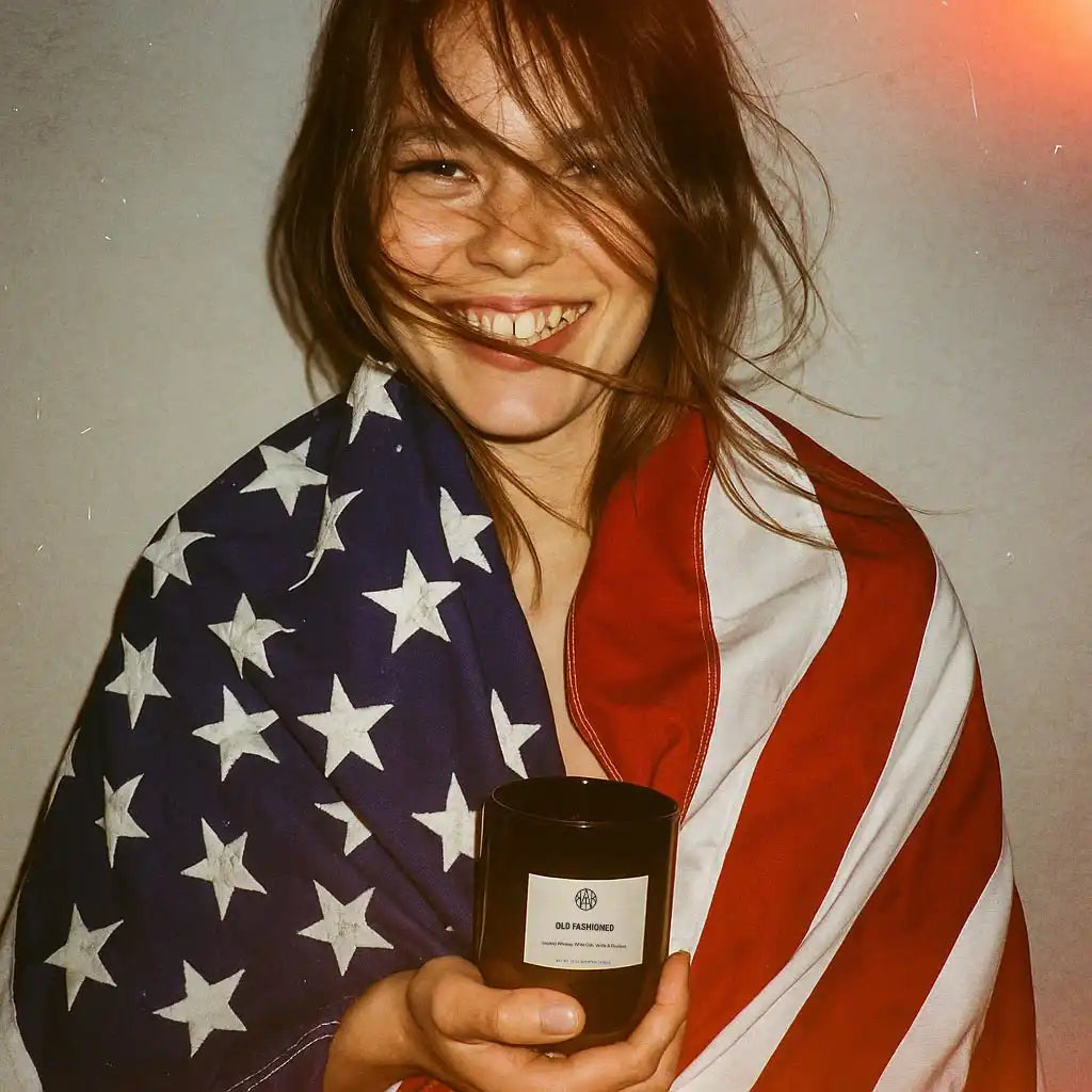 Smiling woman wrapped in American flag holding AEMBR non-toxic Old Fashioned candle