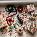 Holiday gift wrapping supplies with AEMBR non-toxic product, ribbons, and festive paper.