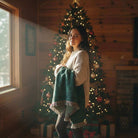 Woman in cozy sweater holding green blanket near decorated Christmas tree in AEMBR-inspired home.