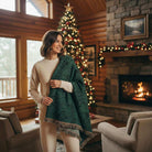 Woman in cozy AEMBR home, wearing cream sweater, with green throw, Christmas tree and fireplace