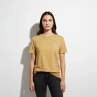 Woman wearing AEMBR tan t-shirt with small white logo, standing against white background