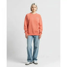 AEMBR model in peach sweatshirt and light blue jeans, standing against a neutral background.
