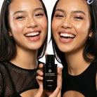 Two women smiling and holding AEMBR ALKYMIST Love Spell fragrance bottle, clean beauty