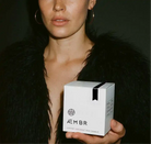 Woman holding AEMBR luxury coconut wax candle box, non-toxic home fragrance brand