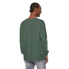 Man wearing green long sleeve shirt with AEMBR logo on sleeve, light denim jeans, white background