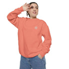 Woman wearing a coral AEMBR sweatshirt with logo, posing against white background