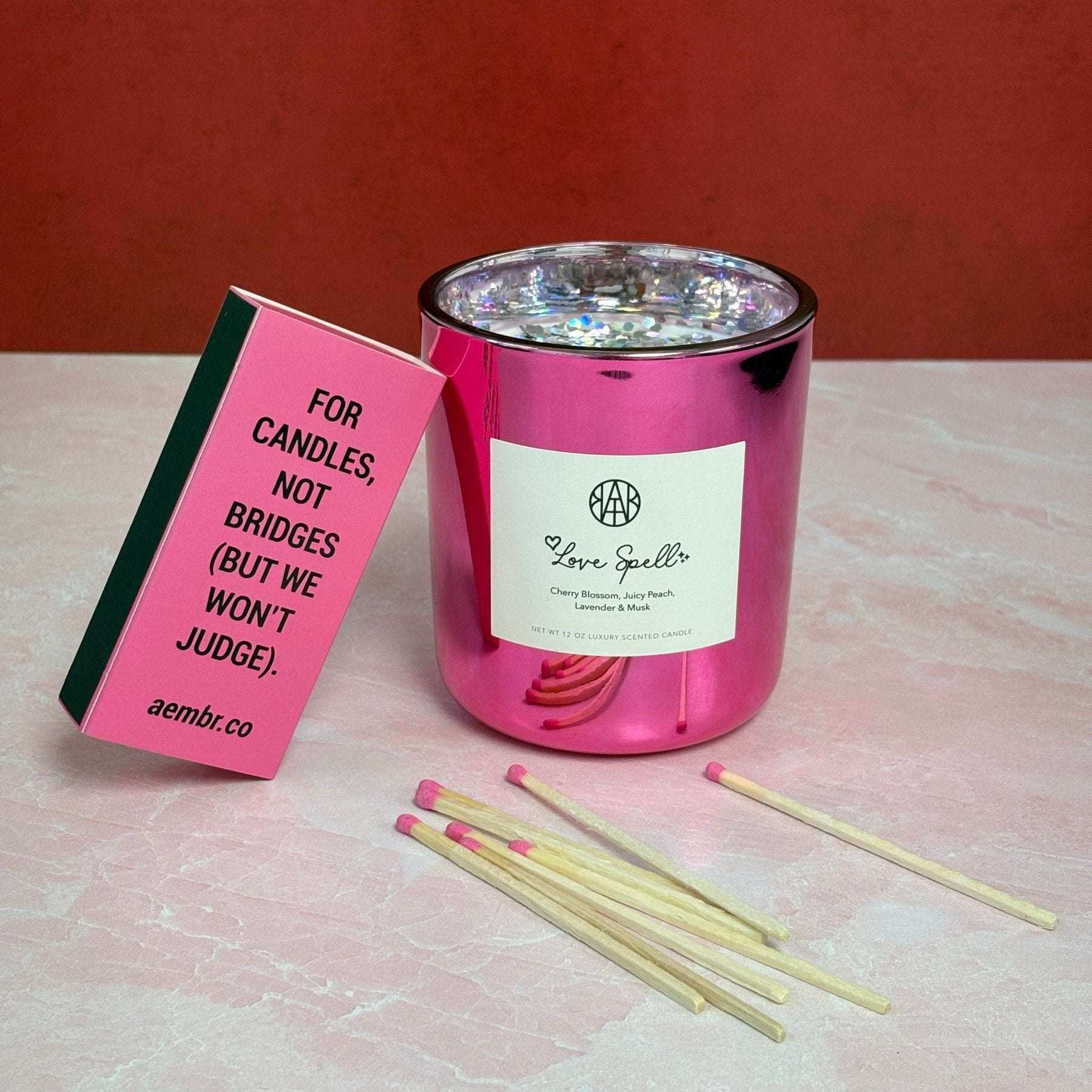 AEMBR pink Love Spell candle with matches and playful matchbox on pink marble surface.