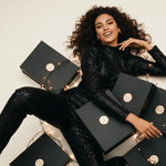 Woman in a black sequin outfit surrounded by black boxes with gold accents on a light background