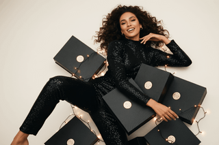 Woman in a black sequin outfit surrounded by black boxes with gold accents on a light background