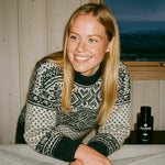 Smiling woman in patterned sweater indoors with ALKYMIST product, cozy natural home setting