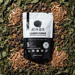 AEMBR non-toxic laundry powder pouch with natural ingredients on leafy background